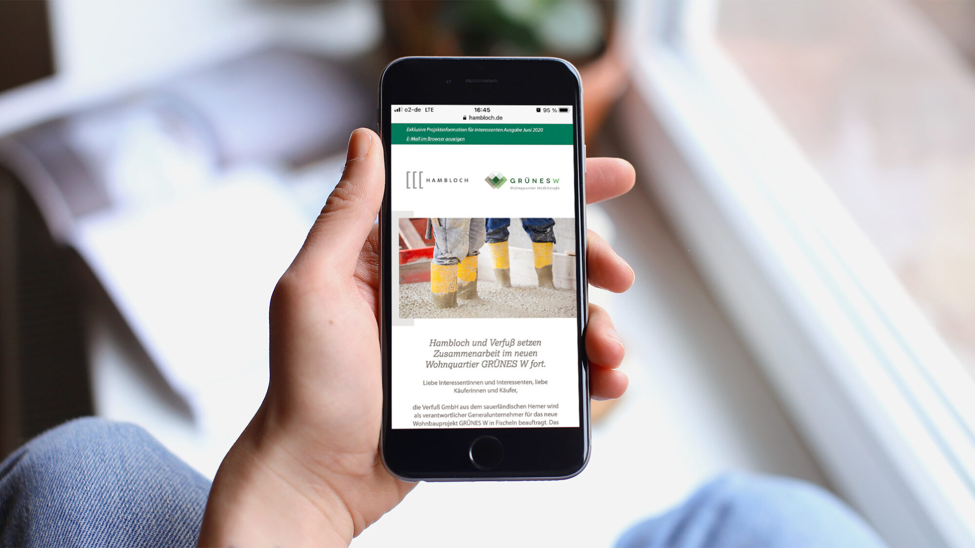 Person hält mit der linken Hand ein iPhone. Auf dem Bildschirm ist der Newsletter des Grünes W Bauprojektes von Hambloch